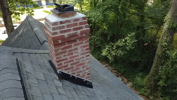 Completed brick chimney masonry and dark roofline flashing viewed from the roof