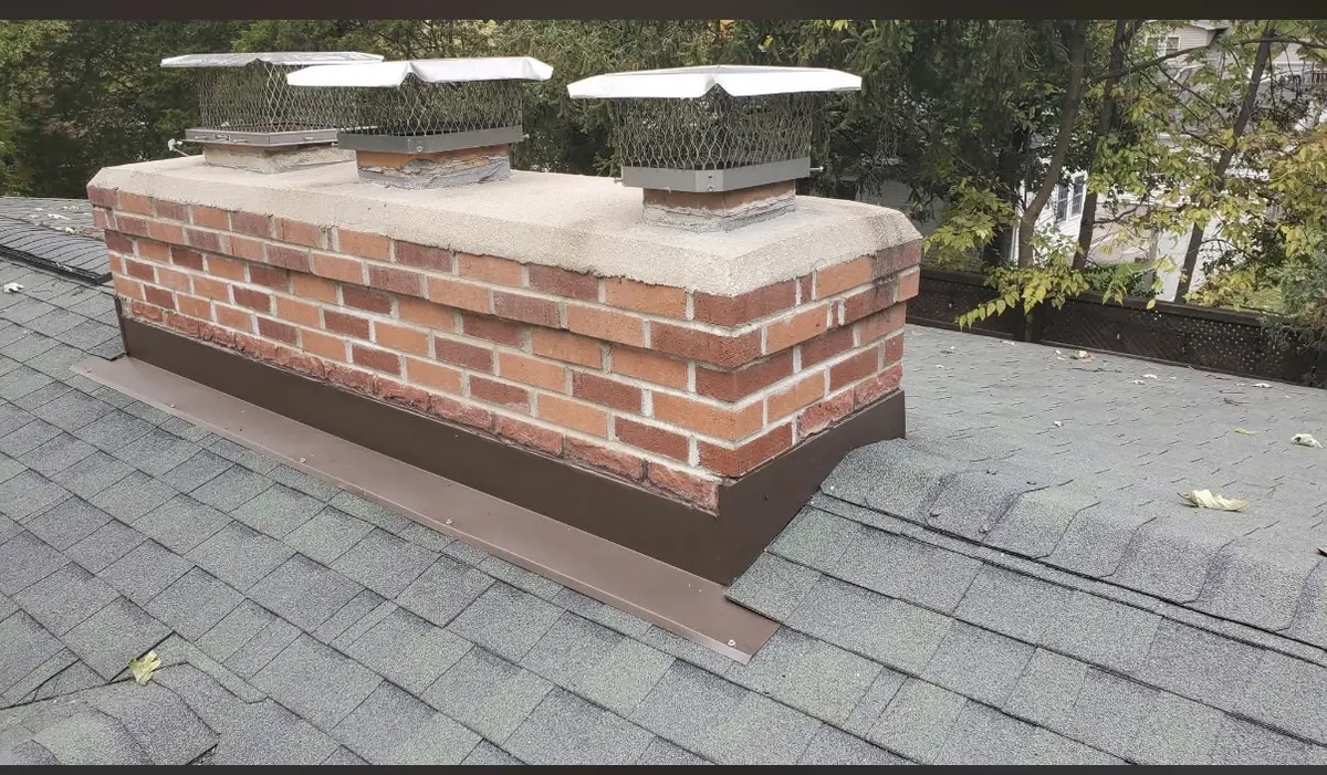 Residential brick chimney top with two metal caps and roofline flashing